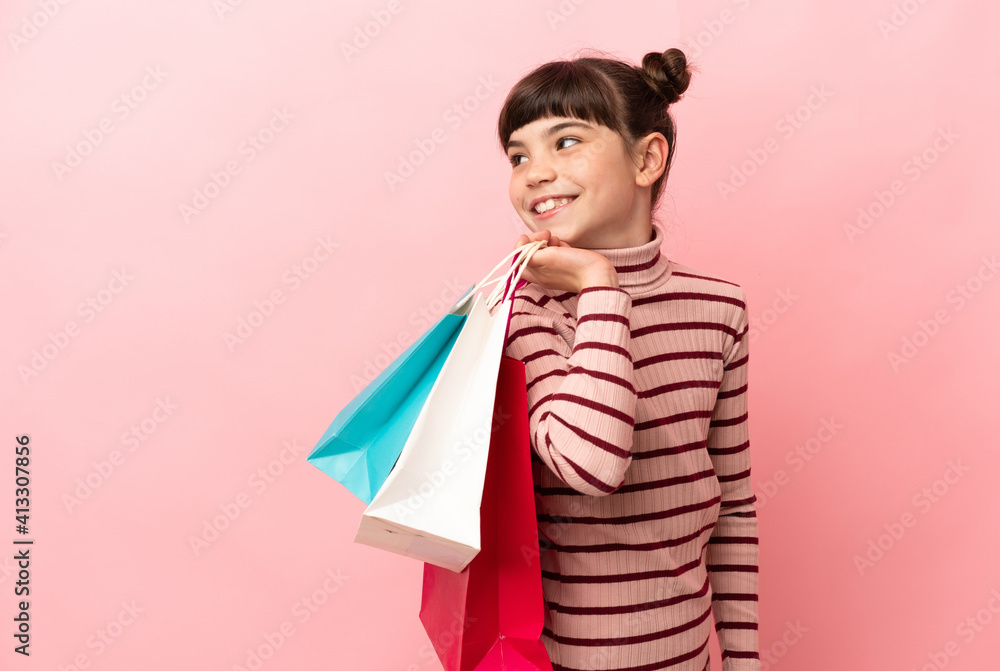 Little caucasian girl isolated on pink background holding shopping bags and looking back Little caucasian girl isolated on pink background holding shopping bags and looking back