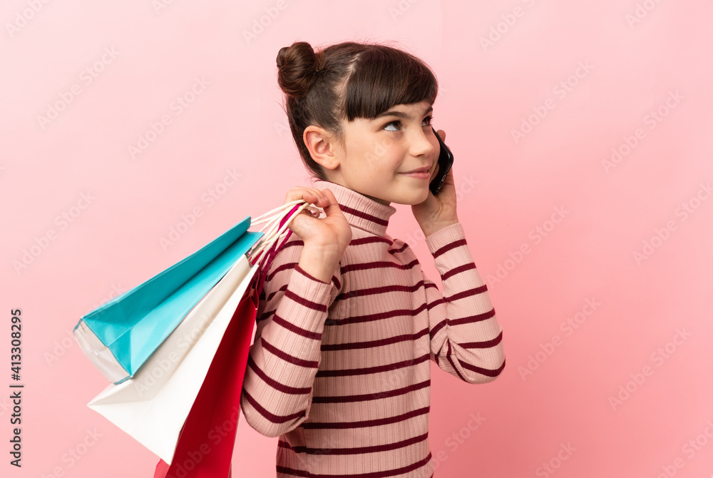 Little caucasian girl isolated on pink background holding shopping bags and calling a friend with her cell phone Little caucasian girl isolated on pink background holding shopping bags and calling a friend with her cell phone
