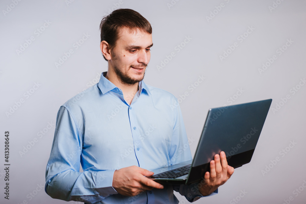A guy in a blue shirt holds a laptop on a white background. Male office worker. Photo in studio A guy in a blue shirt holds a laptop on a white background. Male office worker. Photo in studio