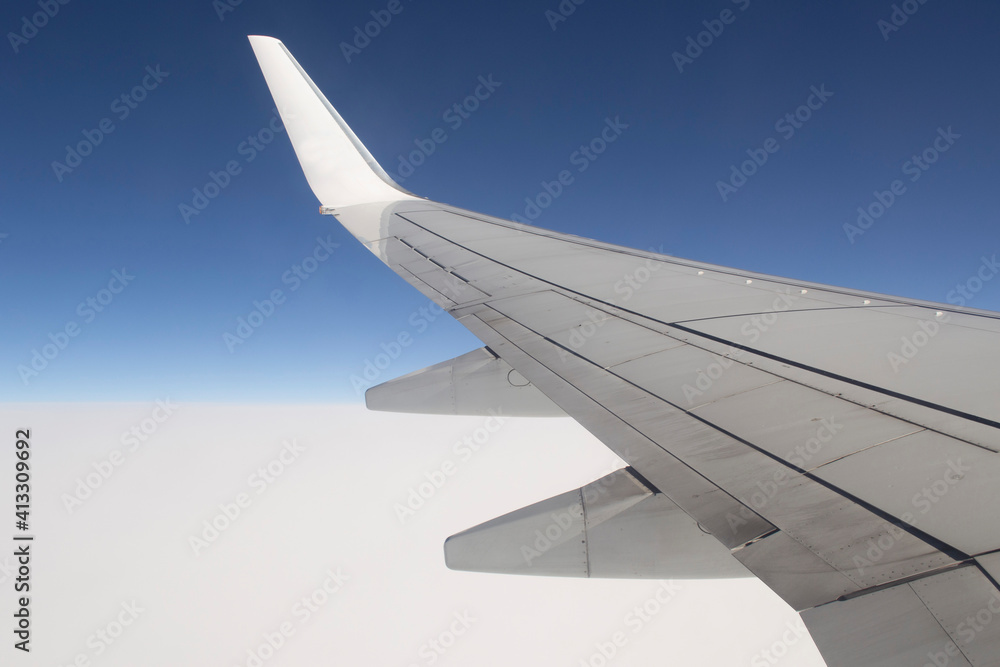 View of an airplane wing, blue sky and a dense layer of white clouds.