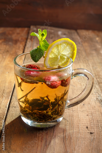green tea in a glass cup with strawberries mint and lemon on a wooden table.