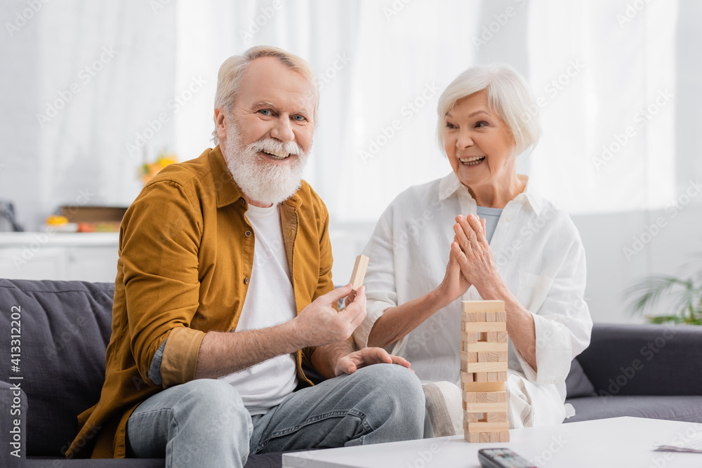 Obraz premium Senior man holding part of blocks wood game near cheerful wife in living room