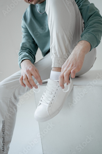 young guy sits and ties the laces on white sneakers