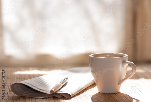 Cup of black coffee, newspaper and a pen against the window in the morning