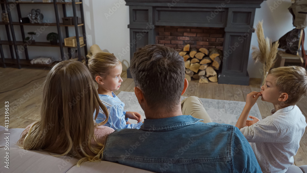 Children sitting near parents on blurred foreground on couch in living room