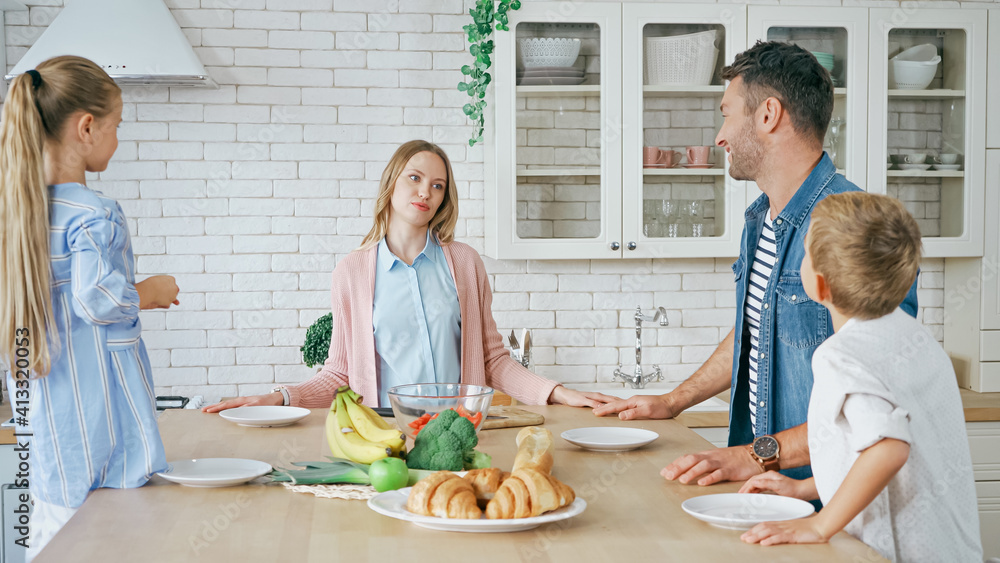 Family on blurred foreground looking at mother near plates and food on kitchen table