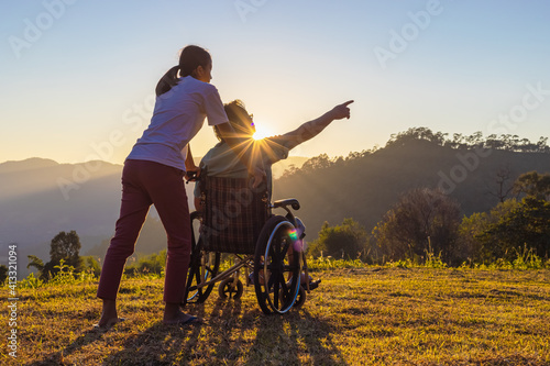 Disabled handicapped man in wheelchair and care helper walking on mountain at sunset.