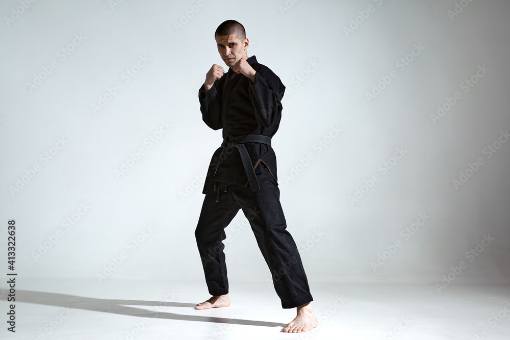 Angry guy trainer in black kimono fighter posing in karate stance on studio background with copy space