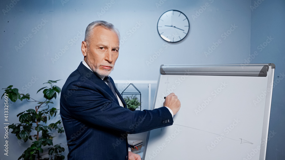 Grey haired businessman drawing on flipchart in office Grey haired businessman drawing on flipchart in office