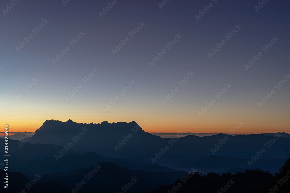 Heaven at early morning with copy space and silhouette mountains.Predawn clear sky with orange horizon and blue atmosphere. Smooth orange blue gradient of dawn sky.