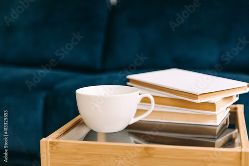 Blank white mug of coffee or tea on a table at home, next to few books.