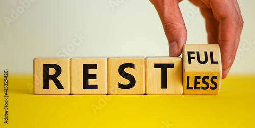Restless or restful symbol. Businessman turns the wooden cube, changes the word 'restless' to 'restful'. Beautiful yellow table, white background, copy space. Business and restless or restful concept.
