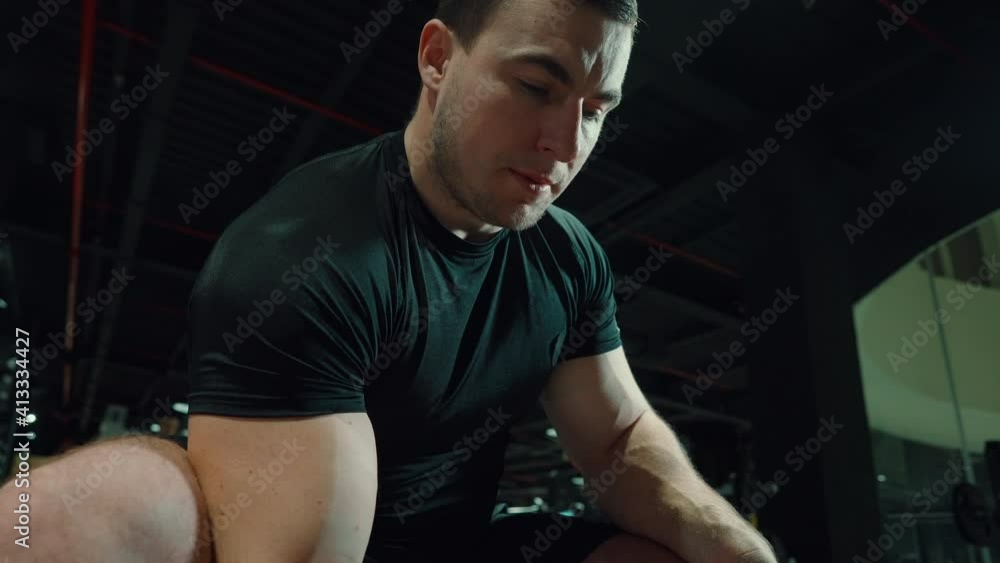 Muscular man in black t-shirt doing biceps exercise with dumbbell in dark gym, unrecognizable people on background. Low angle bodybuilder working out. Concept of sport Muscular man in black t-shirt doing biceps exercise with dumbbell in dark gym, unrecognizable people on background. Low angle bodybuilder working out. Concept of sport