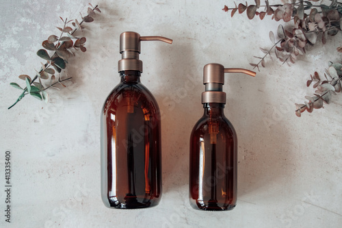 Amber glass shampoo or soap bottle dispenser with a copper steel pump against a stone background. Organic spa cosmetic product with eucalyptus. photo