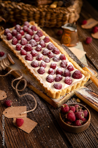 rectangular homemade open short crust pie or tart with white cream and raspberries on wooden white board stands on rustic table, selective focus