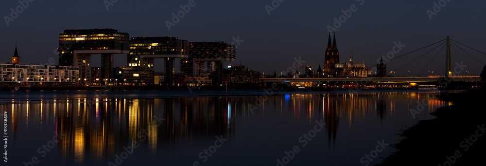 Panorama of Crane houses and Cologne Cathedral by night, iluminated, reflection in the Rhine river