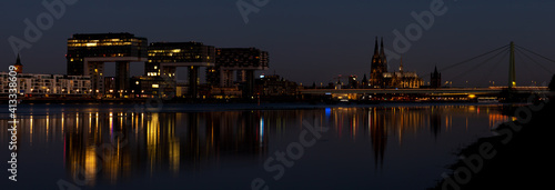 Panorama of Crane houses and Cologne Cathedral by night, iluminated, reflection in the Rhine river