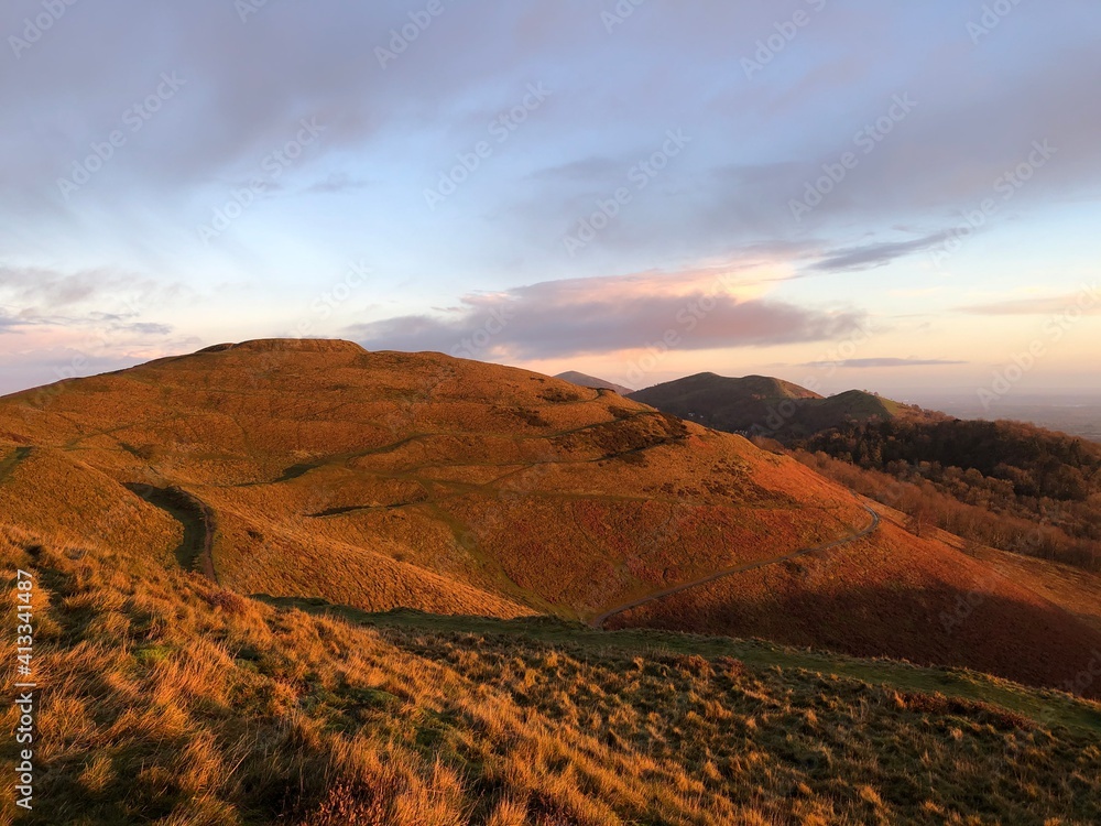 British camp iron age hill fort showing hill ramparts and walking paths at sunrise. Hills leading to Worcestershire beacon in the background.