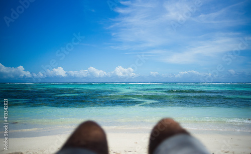 A man lying on the beach looks at the turquoise sea and the blue sky in the Seychelles