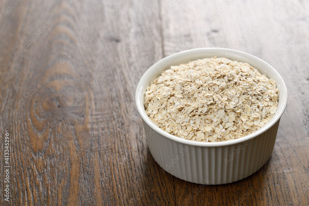 Ceramic bowl of rolled oats on dark stained hickory wood planks Ceramic bowl of rolled oats on dark stained hickory wood planks