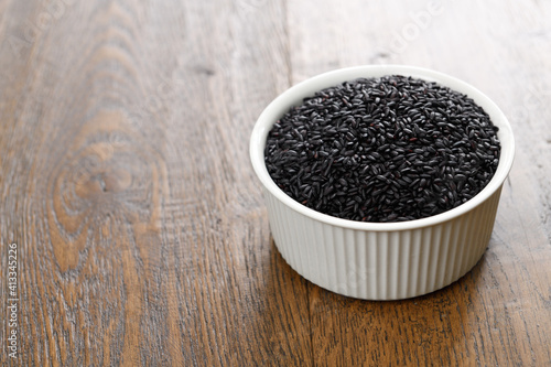 Black rice in a ceramic bowl on stained hickory wood planks