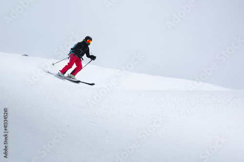 A freerider skier in red pants with a rockzack rides down a snowy slope in cloudy weather. Womens freeride sports background