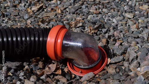 Emptying grey black water tanks flowing through rv hose into septic tank right angle connector. Sewage poop pee dishwater collection disposal.