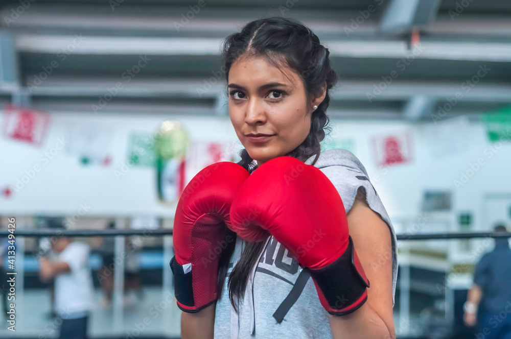 Young attractive latin woman boxer wearing red gloves training on boxing ring.  With a determined expression in a health and fitness concept.