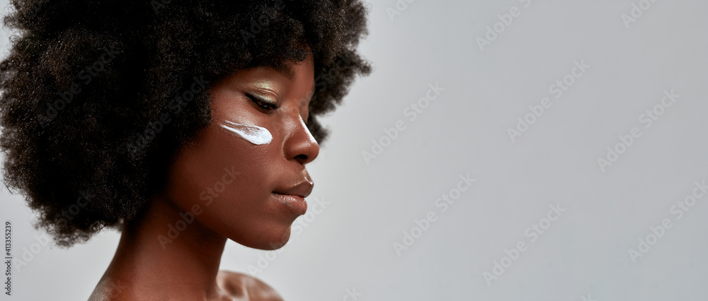 © Svitlana - Cropped portrait of beautiful young half naked african american woman with afro hair looking down while posing with cream applied on her face isolated over gray background