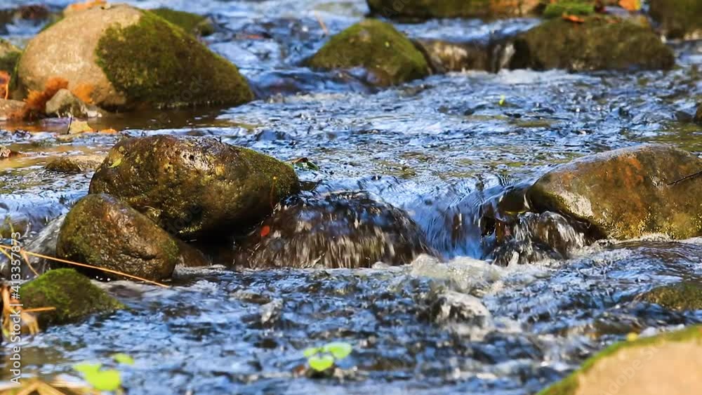 Water running through big stones in water. Close up view mountain stream with  stones. Flowing river with blue water.