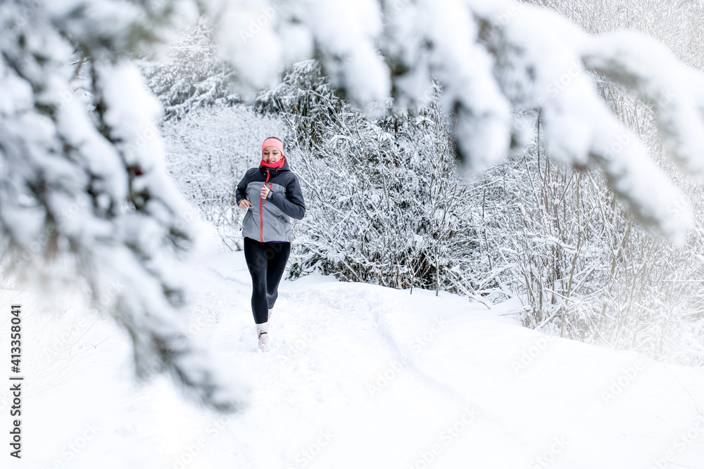 A young happy woman runs in the winter snowy landscape. Sport, fitness inspiration and motivation.