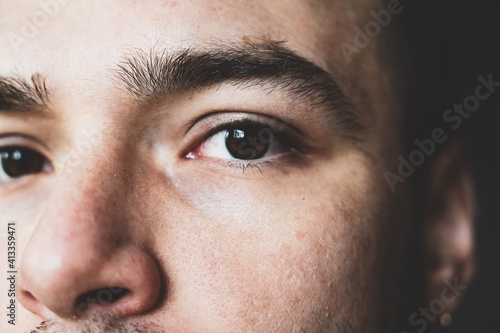 A young man stares at the camera. Brown man's eyes close up. Male face closeup. Lighted male face with small wrinkles and with no bristles.