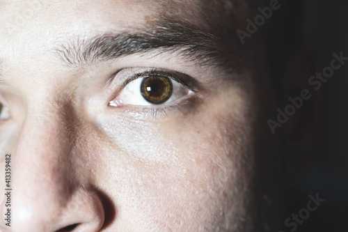 A young man stares at the camera. Brown man's eyes close up. Male face closeup. Lighted male face with small wrinkles and with no bristles.