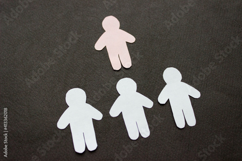 Silhouettes of three men, arranged in a row, cut from paper. Over them there is one pink man. On black background. Concept leadership, communication, power, uniqueness, business photo