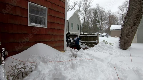 woman and young man struggling to start snow blower in the deep snow in the backyard photo