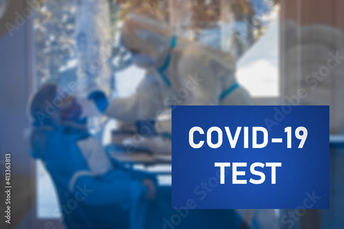 Covid 19 or coronavirus swab test visible in the blurred background with big billboard sign lettering visible in the foreground stating COVID 19 test point. photo