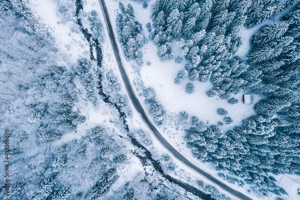 Aerial top view drone shot of the pine and spruce trees forest covered with  snow in the Tatra Mountains in Slovakia with a countryside rural road.  Transportation and ecology concept image. Stock