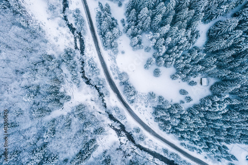 Aerial top view drone shot of the pine and spruce trees forest covered with snow in the Tatra Mountains in Slovakia with a countryside rural road. Transportation and ecology concept image. © Soloviova Liudmyla