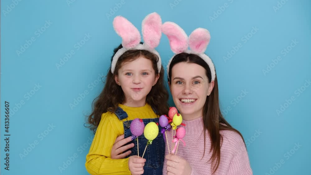 Big day is coming up. Surprised shocked mother with cute daughter to have much work preparation to Easter, holding paints eggs, isolated on blue studio background. Rejoice spring and holidays concept Big day is coming up. Surprised shocked mother with cute daughter to have much work preparation to Easter, holding paints eggs, isolated on blue studio background. Rejoice spring and holidays concept