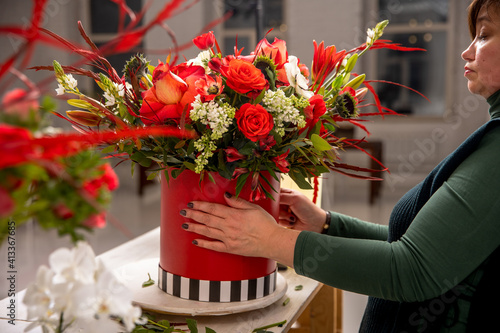 Florist workplace on the background of a white brick wall. A florist examines a floral arrangement of orchids, roses, sunflowers, lilies, alstroemerias and ornithogalums in a red box. Tutorial photo