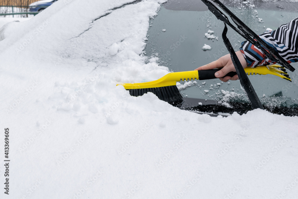 Naklejka premium Man brushing snow and ice from windscreen of car with brush. Person cleaning fresh snow after snowstorm from car in the winter.