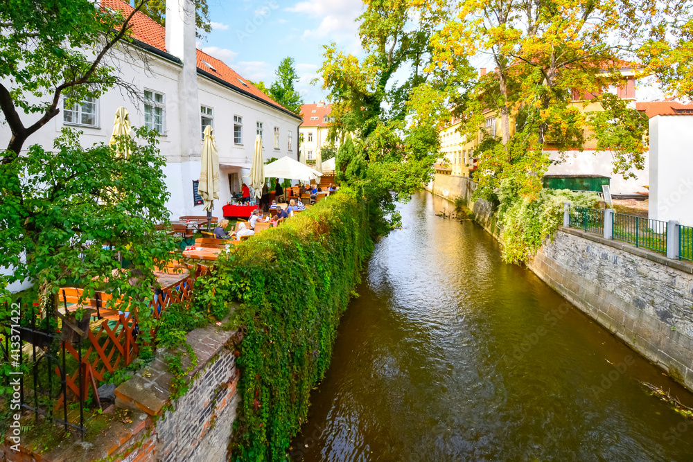 A waterfront cafe with outdoor patio along one of the lush garden canals in the Kampa Island area of Prague, Czechia.