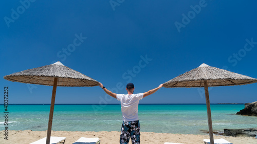 Rear view of young man enjoy holiday by sightseeing on the beach and standing between umbrellas with lifted open hands. Separated  background  cover magazine concept.