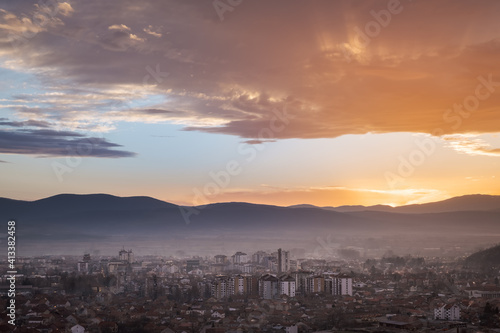 Sun beams shining through the colorful sunset colored clouds over golden lighten city covered by mist
