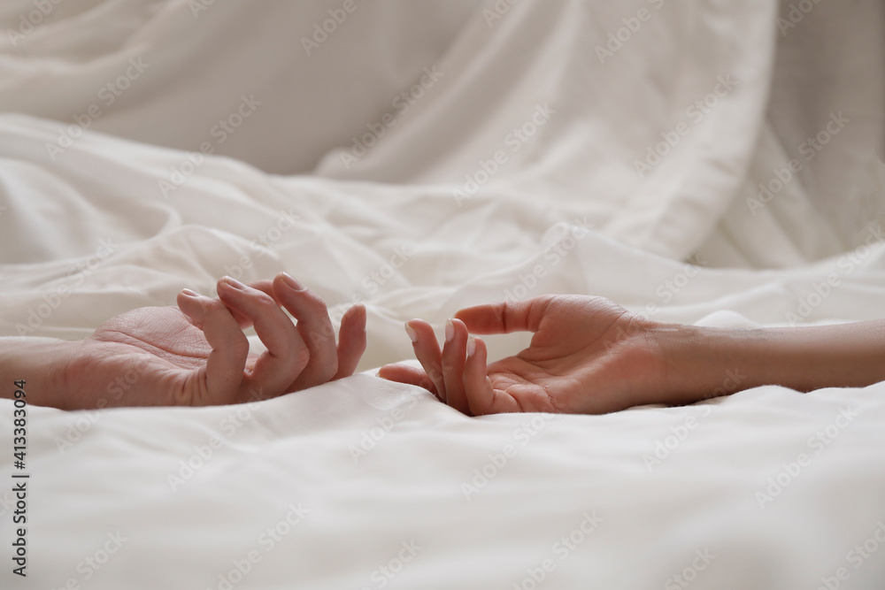 partial view of couple in live holding hads while lying in bed together