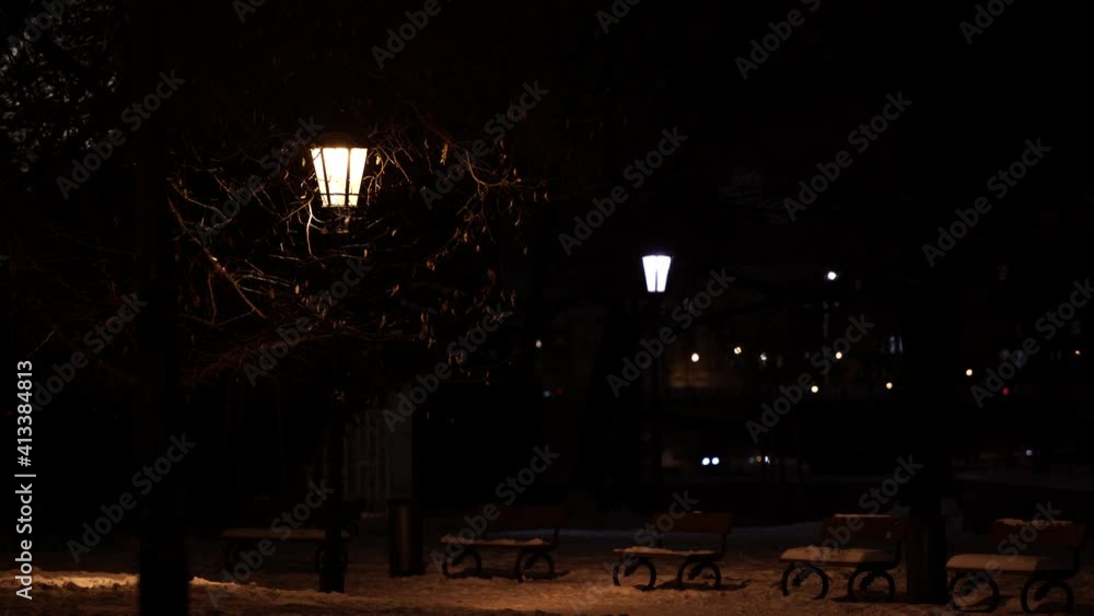 lit street light lantern and snowy sidewalk and park benches and background of world from passing cars in me at night lit street light lantern and snowy sidewalk and park benches and background of world from passing cars in me at night