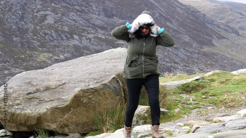 Woman in Welsh mountains struggling to walk in a strong wind and laughing because gale is pushing her back.