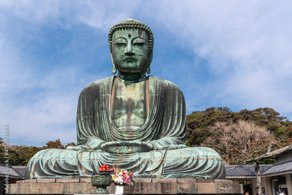 The Great Buddha, Daibutsu, offerings in front, blue sky above in Kamakura, Japan The Great Buddha, Daibutsu, offerings in front, blue sky above in Kamakura, Japan