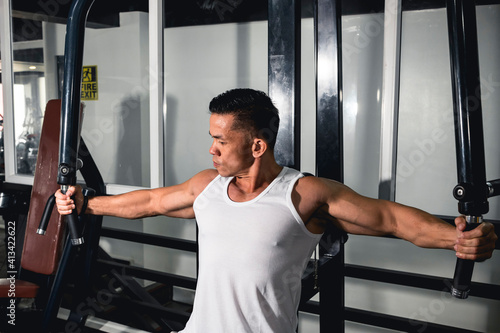 Photos A muscular asian man uses the seated lever fly machine at the gym