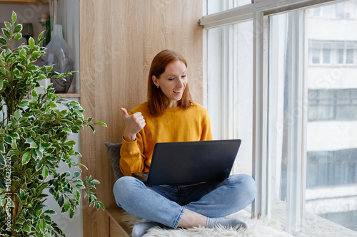 Fotografia An employee or student in a yellow sweater is sitting by the window with a laptop